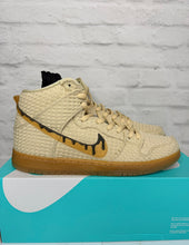 Load image into Gallery viewer, Beige high-top sneakers with brown soles on a blue and white platform against a light gray brick wall.
